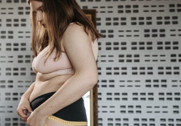 Confident young woman measures her hips in a stylish interior, embracing body positivity.