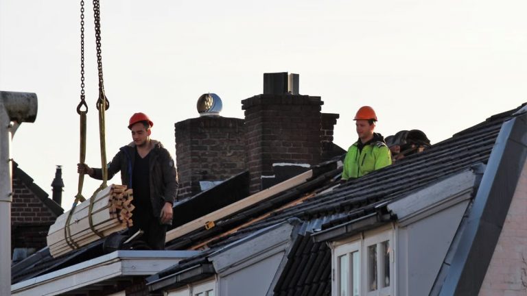 Workers operate on a rooftop under construction in the Netherlands, showcasing teamwork and safety.