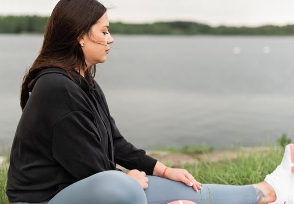 Woman meditating outdoors by a tranquil lakeside, fostering health and wellness.